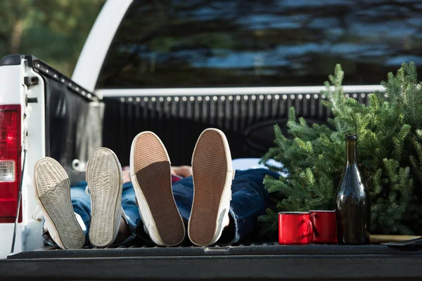 Messa a fuoco selettiva della giovane coppia che posa nel bagagliaio dell'auto con albero di Natale e bottiglia di champagne all'aperto — Foto stock