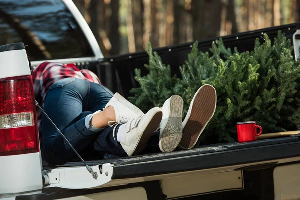 Vista parcial de pareja joven tendida en el maletero del coche con árbol de Navidad y copa al aire libre - foto de stock