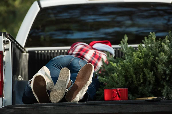 Vue arrière du jeune couple couché dans le coffre de la voiture avec arbre de Noël et tasses à l'extérieur — Photo de stock