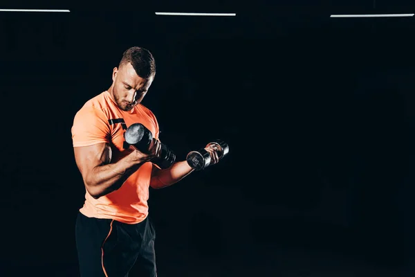 Handsome muscular sportsman working out with barbells in dark gym — Stock Photo