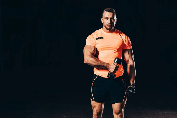 Apuesto deportista atlético haciendo ejercicio con las barras en el gimnasio oscuro - foto de stock