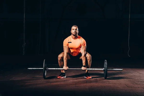 Bonito atlético fisiculturista levantar barbell no escuro ginásio — Fotografia de Stock