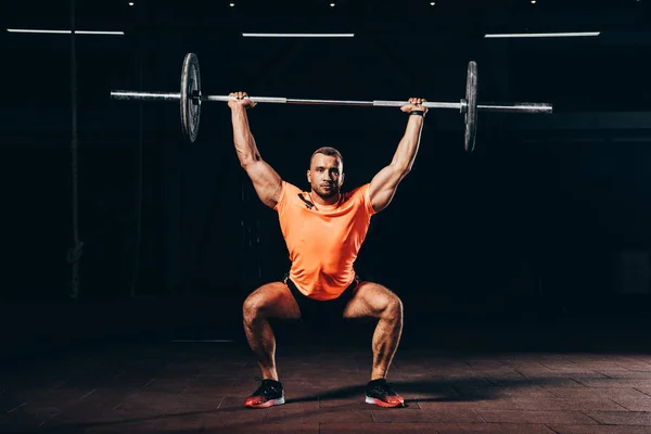 Handsome fit man working out with barbell in dark gym — Stock Photo