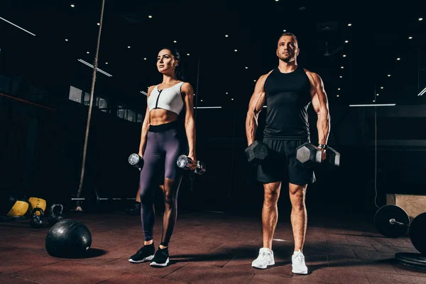 Deportista en forma y deportista haciendo ejercicio con pesas juntos en el gimnasio oscuro — Stock Photo