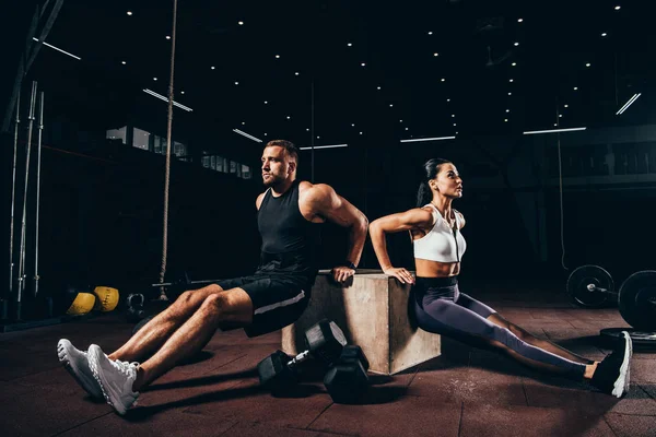 Deportista atlético y deportista haciendo ejercicio en cubo juntos en el gimnasio oscuro - foto de stock