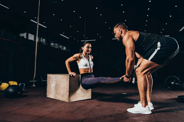 Mujer atlética haciendo ejercicio con entrenador en cubo en el gimnasio oscuro - foto de stock