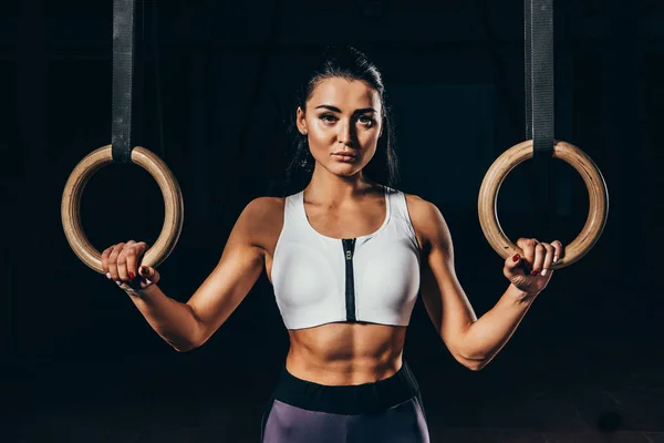 Attractive sporty woman with gymnastic rings looking at camera isolated on black — Stock Photo