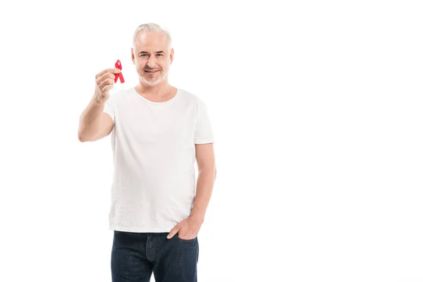 Sorrindo homem maduro em branco t-shirt segurando ajudas consciência fita vermelha e olhando para a câmera isolada no branco — Fotografia de Stock