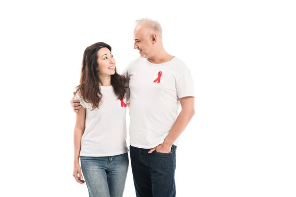 Adult interracial couple in blank t-shirts with aids awareness red ribbons embracing and looking at each other isolated on white — Stock Photo