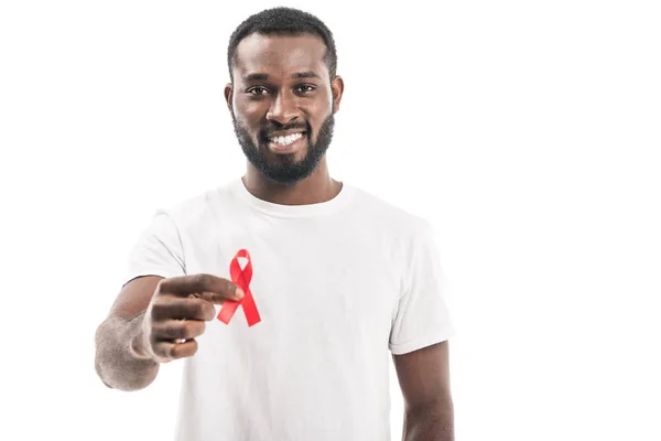 Uomo afroamericano sorridente in bianco bianco t-shirt tenendo aiuti consapevolezza nastro rosso e guardando la fotocamera isolata su bianco — Foto stock