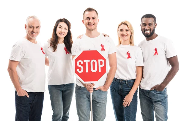Group of people in blank white t-shirts with aids awareness red ribbons and stop road sign looking at camera isolated on white — Stock Photo