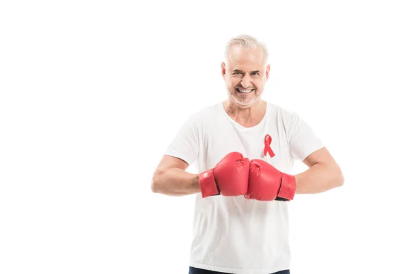 Homme mûr souriant en t-shirt blanc vierge avec des gants de boxe et un ruban rouge de sensibilisation au sida isolés sur du blanc, concept d'aide au combat — Photo de stock