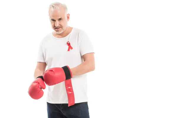Serious mature man in blank white t-shirt with aids awareness red ribbon and boxing gloves isolated on white, fighting aids concept — Stock Photo