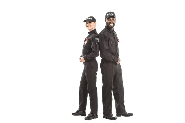 Улыбающиеся офицеры полиции с красными лентами, смотрящие в камеру, стоя спиной к спине, изолированные на белом — стоковое фото