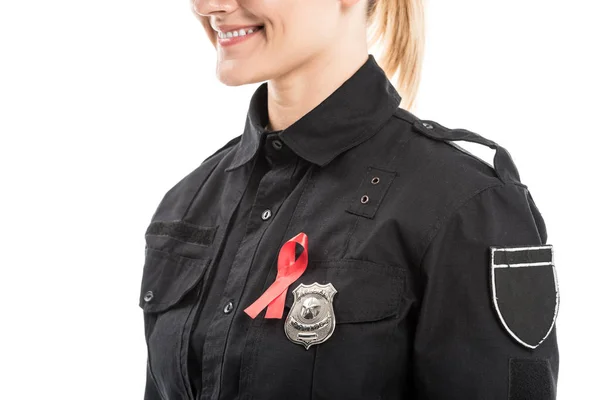 Recortado disparo de sonriente oficial de policía femenino con SIDA cinta roja conciencia aislado en blanco - foto de stock