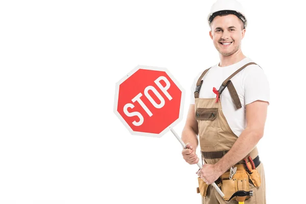 Costruttore adulto sorridente con aiuti consapevolezza nastro rosso sul cartello stradale arresto generale tenuta e guardando la fotocamera isolata su bianco — Foto stock