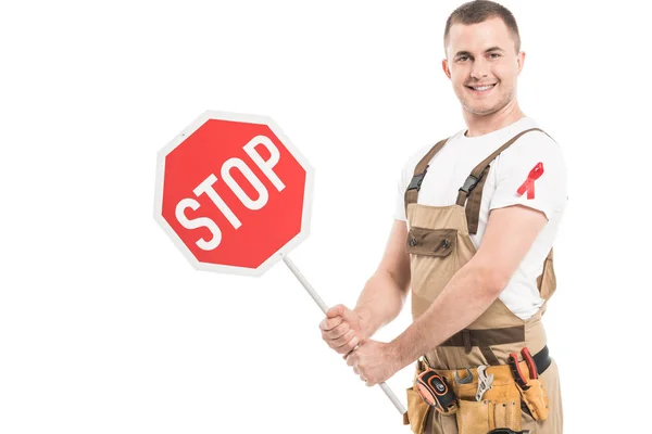 Constructor adulto feliz con ayuda a la conciencia cinta roja en la celebración general señal de stop road y mirando a la cámara aislada en blanco - foto de stock