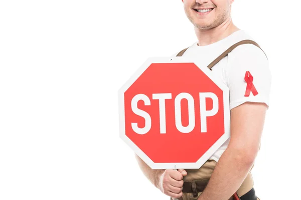 Abgeschnittene Aufnahme eines lächelnden Bauunternehmers mit Hilfsmitteln Bewusstsein rotes Band auf Gesamt Halten Stopp-Straßenschild isoliert auf weiß — Stockfoto