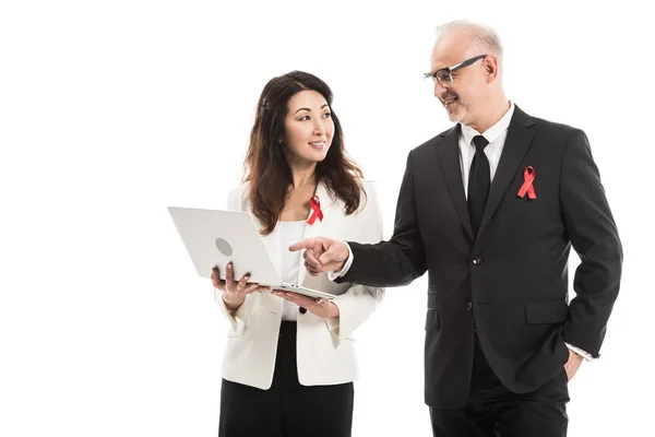Heureux hommes d'affaires adultes multiethniques avec des rubans rouges de sensibilisation au sida travaillant ensemble avec ordinateur portable isolé sur blanc — Photo de stock