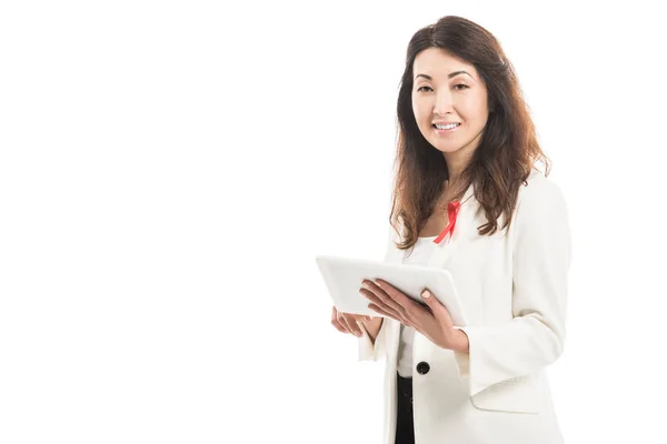 Sourire asiatique femme d'affaires avec sida sensibilisation ruban rouge sur la veste à l'aide d'une tablette et en regardant la caméra isolée sur blanc — Photo de stock