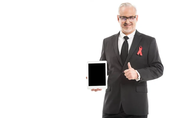 Maduro hombre de negocios en traje con SIDA conciencia cinta roja celebración de la tableta con pantalla en blanco y mostrando el pulgar hacia arriba aislado en blanco - foto de stock