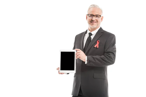 Maduro hombre de negocios en traje con SIDA conciencia cinta roja celebración tableta con pantalla en blanco aislado en blanco - foto de stock