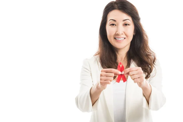 Улыбающаяся азиатская бизнесвумен, держащая в руках красную ленту и смотрящая на камеру, изолированную на белом — стоковое фото