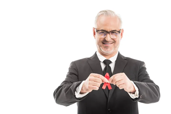 Зрелый бизнесмен в костюме держит вспомогательные средства осведомленности красная лента и глядя на камеру изолированы на белом — стоковое фото