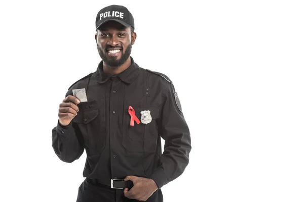 Усміхнений афроамериканський поліцейський з поінформованістю про червону стрічку, що тримає презерватив ізольовано на білому — стокове фото