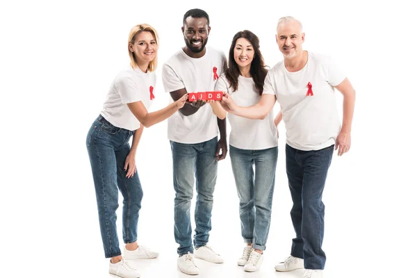 Група багатоетнічних людей у чистих білих футболках зі свідомістю червоних стрічок, що тримають блоки зі СНІДом, ізольовані на білому — стокове фото