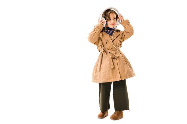 Beau petit enfant en trench coat avec écouteurs isolés sur blanc — Photo de stock