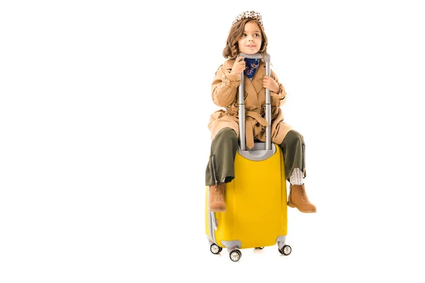 Adorable petit enfant en trench coat assis sur valise jaune isolé sur blanc — Photo de stock