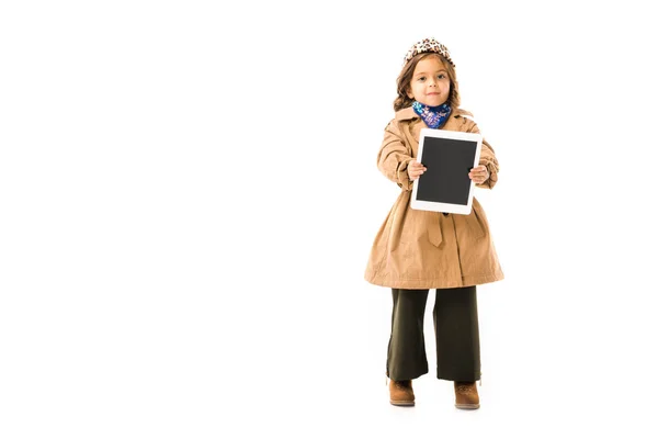 Hermoso niño pequeño en gabardina mostrando tableta con pantalla en blanco aislado en blanco - foto de stock