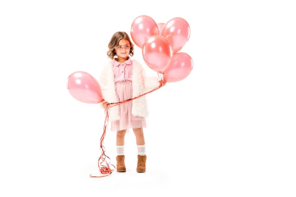 Niño pequeño con estilo en abrigo de piel con globos de aire de color rosa aislado en blanco - foto de stock