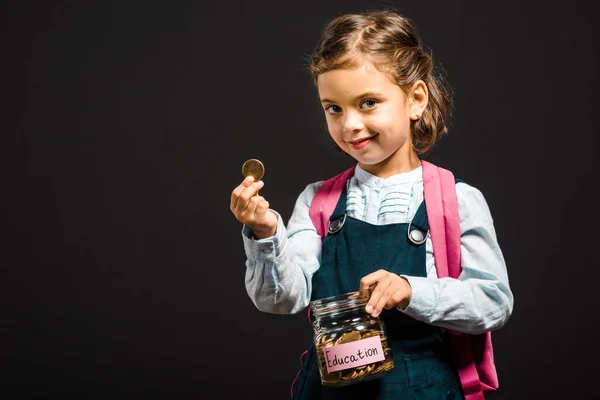 Scolaretta con zaino contenente vaso di vetro con risparmi per l'istruzione isolato su nero — Foto stock