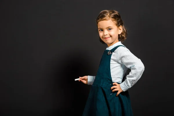 Smiling schoolgirl with piece of chalk standing at blank blackboard — Stock Photo