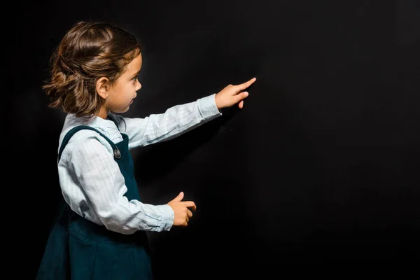 Cute schoolgirl pointing at blank blackboard — Stock Photo