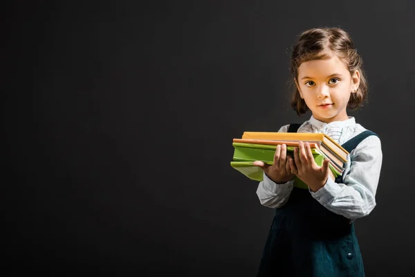 Portrait d'adorable écolier tenant des livres isolés sur noir — Photo de stock