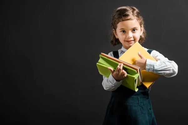 Portrait of adorable schoolgirl holding books isolated on black — Stock Photo