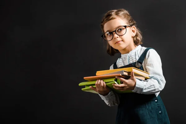 Porträt eines entzückenden Schulkindes mit Brille und Büchern auf Schwarz — Stockfoto