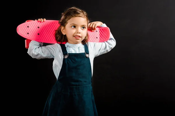 Portrait of cute schoolchild holding pink penny board isolated on black — Stock Photo