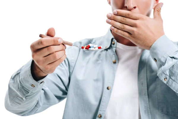 Abgeschnittenes Bild eines Mannes, der den Mund bedeckt und einen Löffel Pillen auf weiß isoliert hält — Stockfoto