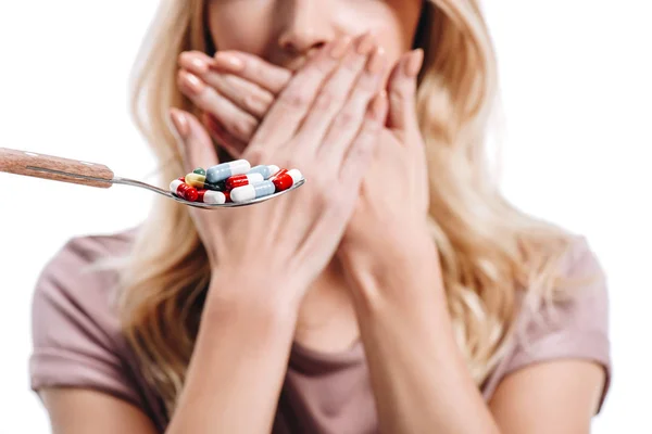 Cropped image of woman covering mouth in front of spoon of pills isolated on white — Stock Photo