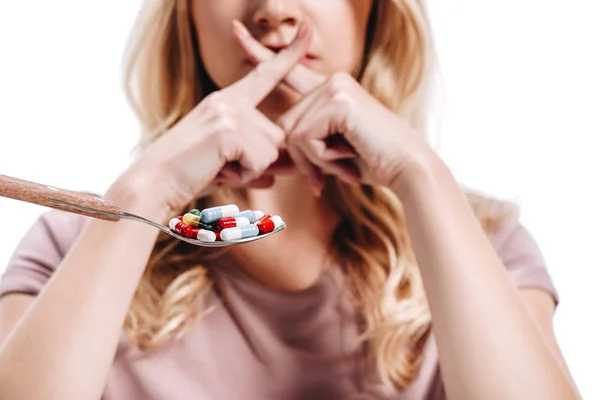 Cropped image of woman covering mouth with fingers in front of spoon of pills isolated on white — Stock Photo