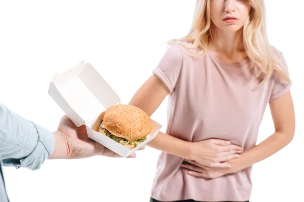 Cropped image of blonde woman showing stomach pain, man proposing unhealthy burger isolated on white — Stock Photo