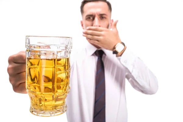 Messa a fuoco selettiva dell'uomo d'affari che copre la bocca e che tiene il vetro di birra malsana isolato su bianco — Foto stock