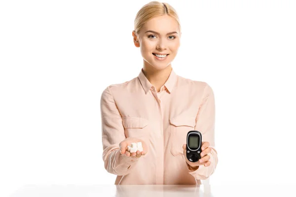 Attractive smiling blonde woman holding refined sugar and glucometer isolated on white, diabetes concept — Stock Photo