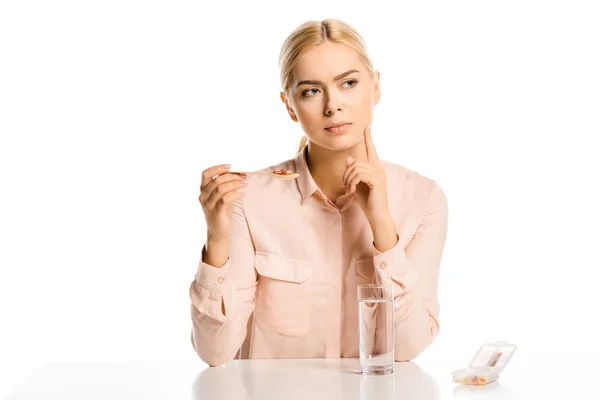 Приваблива смілива жінка тримає ложку таблеток і дивиться ізольовано на білому — стокове фото