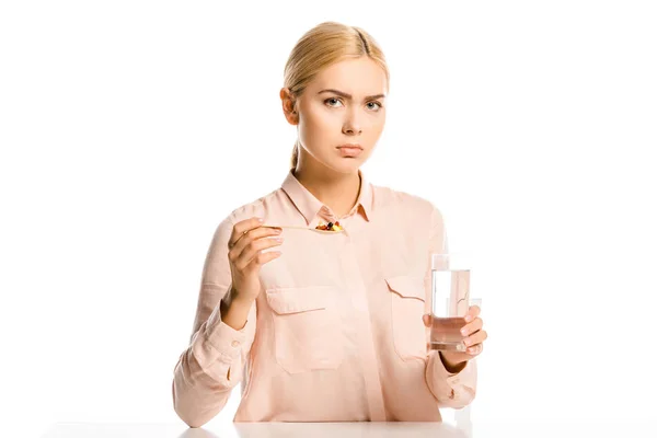 Irritado atraente mulher segurando colher de comprimidos e vidro de água isolado em branco — Fotografia de Stock