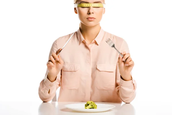 Приваблива жінка зі стрічкою міра на очах готова їсти брокколі ізольовані на білому — стокове фото